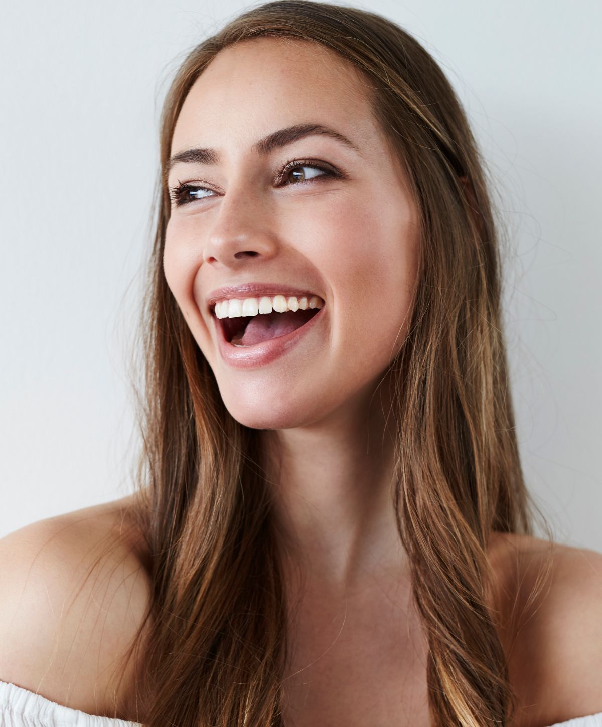 Smiling woman with long hair against white wall