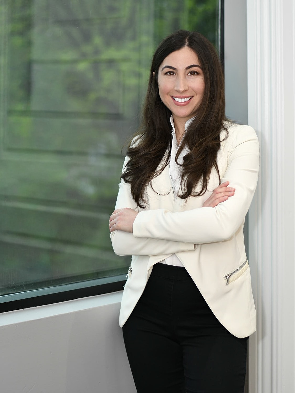 Businesswoman standing by a window, smiling confidently.