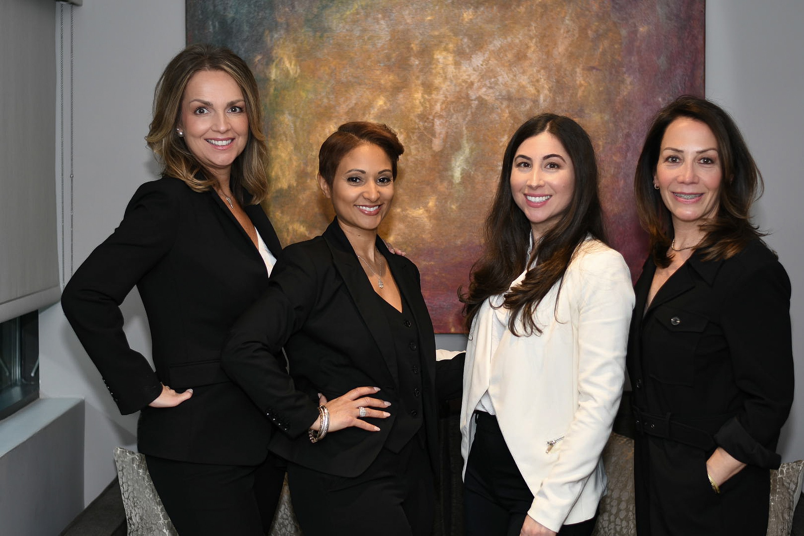 Four women in professional attire smiling together.